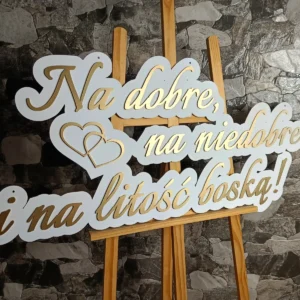 Elegancki napis dekoracyjny w stylu glamour w kolorach bieli i złota to idealne dopełnienie ślubnej ścianki. Subtelny blask złotych detali w połączeniu z klasyczną bielą tworzy wyjątkowo luksusowy efekt, który przyciąga wzrok i pięknie prezentuje się na zdjęciach. To stylowy akcent, który doda Waszej uroczystości wyjątkowej klasy i romantycznego klimatu.